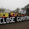 Protesters dressed in jump suites hold a banner that says "close Guantanamo"