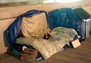 An elaborate outdoor sleeping encampment on a Toronto sidewalk. A cardboards sign says 'I'm very hungry'.  